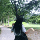 a woman is walking down a path in a park with a black bag that says supreme on it