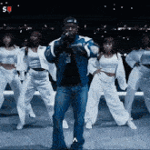 a man in a blue jacket is surrounded by a group of dancers