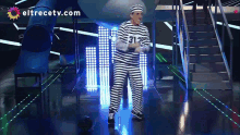 a man in a striped prison uniform is dancing on a stage in front of eltrecetv.com