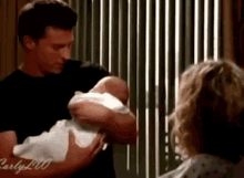 a man is holding a baby in his arms next to a woman in a hospital gown .