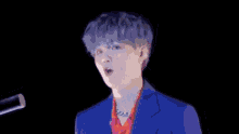 a young man in a blue suit is singing into a microphone in front of a black background .