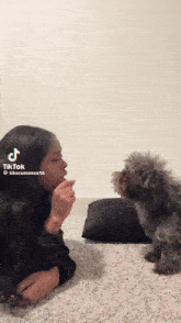 a woman is laying on the floor with a small dog looking at her