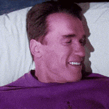 a man in a purple shirt is laying on a bed and smiling .