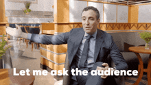 a man in a suit and tie is sitting in a chair and says " let me ask the audience "