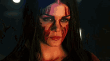 a woman with blood on her face is standing in front of a crowd of people holding guns .