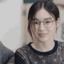 a woman wearing glasses and a floral shirt smiles