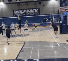 a group of people playing volleyball in front of a sign that says wolfpack fans family