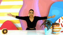 a woman is sitting at a table with her arms outstretched in front of a plant and donuts