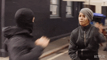 a woman wearing a beanie and a black jacket is being attacked by a man wearing a mask ..