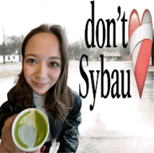 a woman holding a cup of green tea in front of a sign that says " do n't sybau "