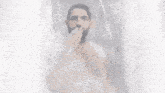 a shirtless man with a beard is taking a shower under a waterfall