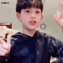 a young boy wearing a black hoodie is giving a thumbs up sign .