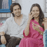 a man and woman are sitting on a couch and the woman is covering her nose