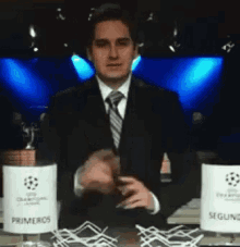 a man in a suit and tie stands in front of a table with two primeros and seguros signs on it