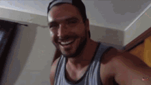 a man wearing a hat and a tank top is smiling in a room .