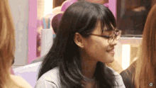 a woman wearing glasses and earrings is smiling in a room with other women .