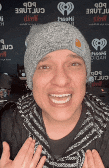 a man wearing a gray beanie is smiling in front of a wall that says iheartradio