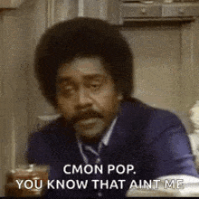 a man in a suit and tie is sitting at a table in a kitchen talking to someone .