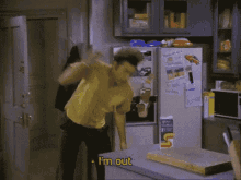 a man in a cowboy hat is standing at a table in front of a refrigerator and saying i 'm out .