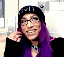 a woman with purple hair and glasses is wearing a black beanie .