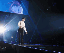 a man stands on a stage with a large screen behind him that says ' spjm '
