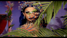 a woman with a crown on her head holds a palm tree leaf in front of her face