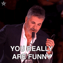a man in a suit is holding a pair of glasses in front of a microphone and says " you really are funny "