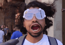 a man wearing goggles and a white shirt has his mouth open