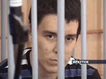 a man in a striped shirt is behind bars in a prison cell