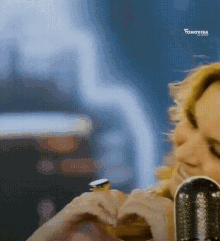 a woman making a heart with her hands in front of a microphone