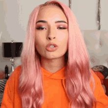 a woman with long pink hair is wearing an orange hoodie and making a funny face .