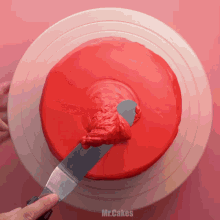 a person spreading red frosting on a cake with a spatula