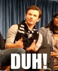 a man and a woman are sitting in front of a blue curtain with the word duh in white