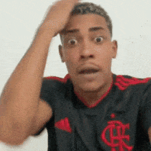 a man wearing a black and red adidas shirt is making a surprised face .
