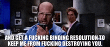 a bald man with glasses is talking on a cell phone while another man stands behind him .