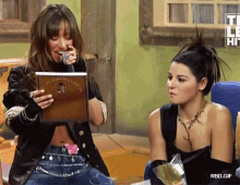 two women are sitting next to each other and one is holding a microphone while the other looks at a picture ..