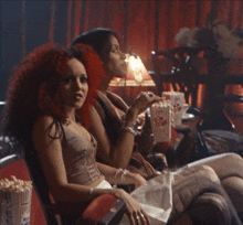 two women sitting in a theater eating popcorn