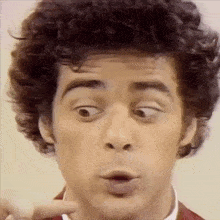 a man with curly hair is making a funny face while pointing at something .