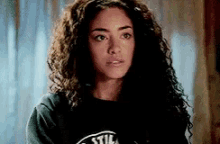 a woman with curly hair is wearing a black t-shirt with a logo on it .