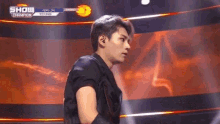 a man is standing on a stage with a microphone in his hand and looking at the camera .