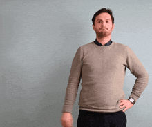 a man wearing a grey sweater and black pants is standing with his hands on his hips