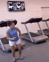 a woman is dancing on a treadmill in a gym with a tv above her