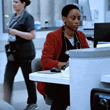 a woman with a stethoscope around her neck sits at a desk