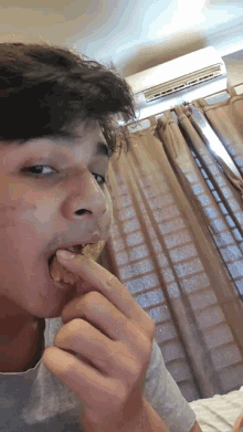 a young man eating a piece of food in front of a window