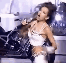 a woman is singing into a microphone while dancing in front of a motorcycle .