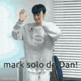 a man in a white sweater is standing in front of a window and waving his hands .