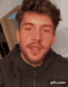 a young man with a beard and a red spot on his forehead is looking at the camera .
