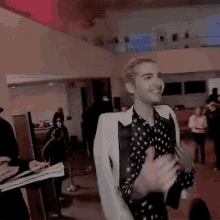 a man in a black and white polka dot shirt and white jacket is standing in a room .