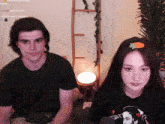 a man and a woman are sitting next to each other with a ladder in the background and a woman has a carrot hair clip