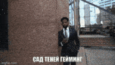 a man in a suit and tie is standing in front of a building with the words " сад тени гейминг " written on the bottom